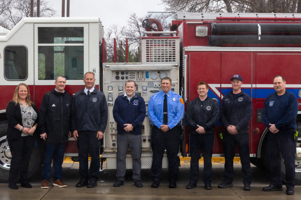 Group photo of Iowa Western Community College and Council Bluffs Fire Department representatives standing in front of a donated red fire engine in Council Bluffs, IA.